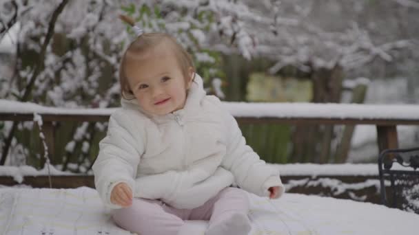 Feliz menina sorridente sentada no parque de neve. Criança desfrutando da primeira neve . — Vídeo de Stock