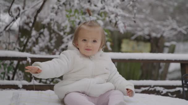 Glad leende liten flicka sitter i Snow Park. Liten unge njuter av den allra första snön. — Stockvideo