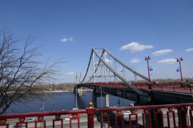 Mavi bahar gökyüzüne karşı. Şehirden küçük bir adaya uzanan geniş bir nehir üzerinde çok büyük bir yaya-bisiklet köprüsü değil..