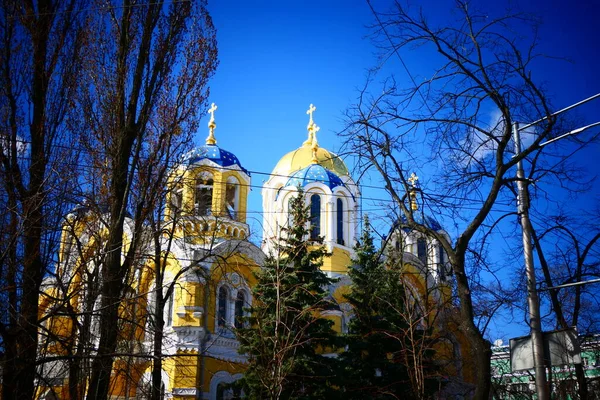 The magnificent building of the yellow Orthodox church with white stucco and blue domes, located next to the old park.