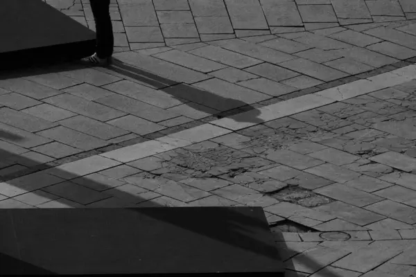 記念碑の台座の横に白いスニーカーで男の足だけでなく 花崗岩の正方形の男の全体の影 — ストック写真
