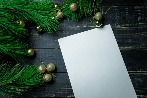 Noel tatili arkaplanı. Siyah tahta bir masa ve beyaz bir çarşaf. Yeni yıl çamı ve altın Noel baloları. Üst Manzara. Metin için yer.