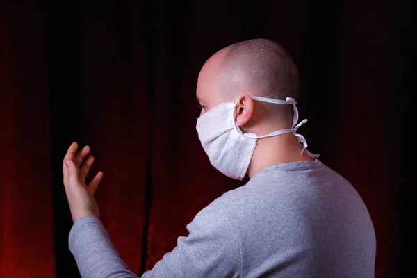 Profile of a man in medical gauze mask standing on dark red background. Protection of upper and lower respiratory tract from coronavirus. Virus preventive action concept.