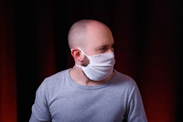 Koyu kırmızı arka planda duran tıbbi gazlı bez maskeli bir adam. Virüs önleyici yöntemler. Üst ve alt solunum sisteminin Çin koronavirüs kavramından korunması.