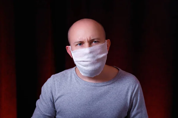 Koyu kırmızı arka planda duran, tıbbi gazlı bez maskeli, kaşları çatık bir adam. Çaresizlik duygusuyla. Virüs önleyici yöntemler. Üst ve alt solunum sisteminin Çin koronavirüs kavramından korunması.