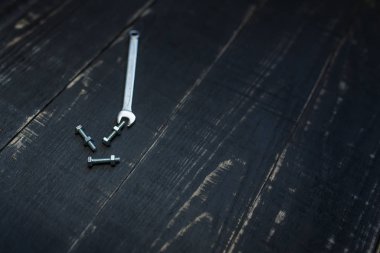 Çift taraflı anahtar, siyah ahşap arka planda biraz somun ve cıvata. Profesyonel aletler, garaj ekipmanları, metal aletler. Metin için yer.