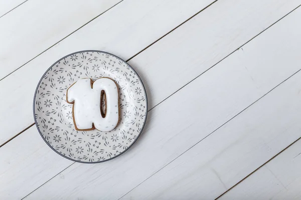 Number 10 shape gingerbread cookie on plate standing on white wooden table background. Number ten concept. Place for text.