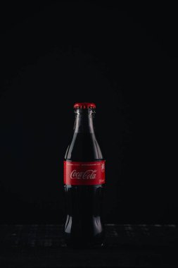 İzmail, Ukrayna - 13 Mart 2020. Siyah arka planda Coca Cola şişesi. Ahşap masada bir şişe kola..
