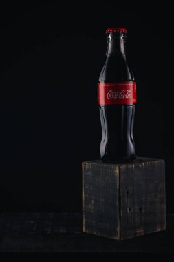 İzmail, Ukrayna - 13 Mart 2020. Siyah arka planda Coca Cola şişesi. Ahşap masada bir şişe kola..
