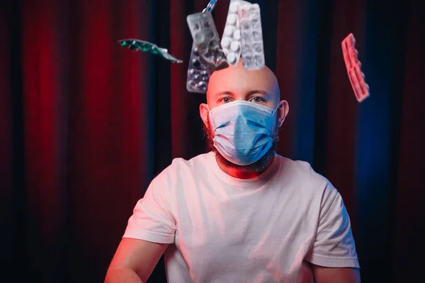 Man in gauze mask and flying medicines on dark red and blue background. Healthcare, respiratory illness prevention, prophylaxis of virus infections, COVID-19 concept.