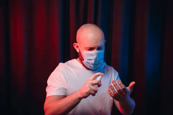 Man in gauze mask holding disinfection spray and sprinkling sanitizer on hands. Healthcare, respiratory illness prevention, prophylaxis of virus infections, COVID-19 concept.