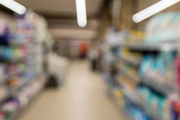 Unfocused shot of supermarket interior. Blurry hypermarket, mall or shopping center background. Rows and shelves with household chemicals and hygiene products.