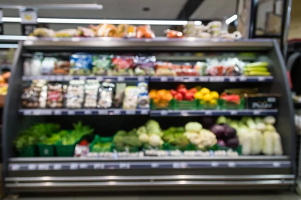 Süpermarketin iç mekanının odaklanmamış görüntüsü. Bulanık hipermarket, alışveriş merkezi ya da alışveriş merkezi geçmişi. Taze yeşillik ve sebzelerle dolu sıra sıra marketler ve raflar..
