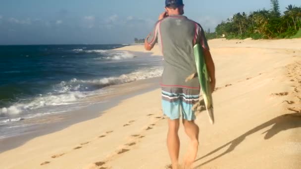 Серфер с доской для серфинга и прогулка по пляжу Гавайев — стоковое видео