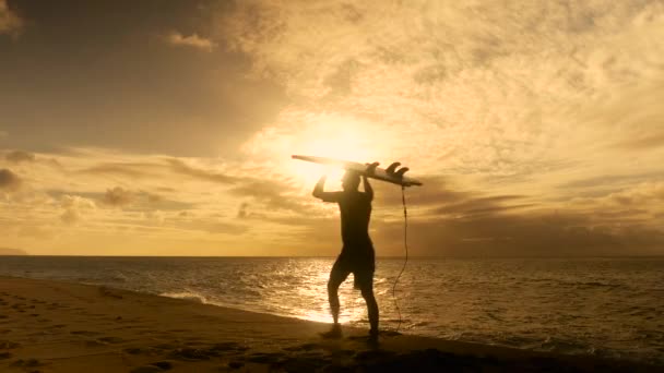 Surfař drží surfovací prkno a chůze po pláži při západu slunce — Stock video