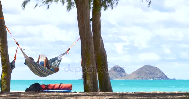 Ung man en bok på hängmatta exotisk strand — Stockvideo