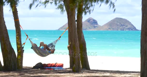 ハンモック エキゾチックなビーチで本を読んでいる若い男の人 — ストック動画