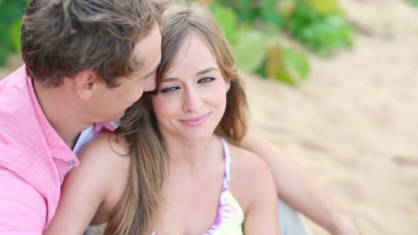 Sonriente joven pareja enamorada, sentada y abrazada en la playa — Vídeo de stock