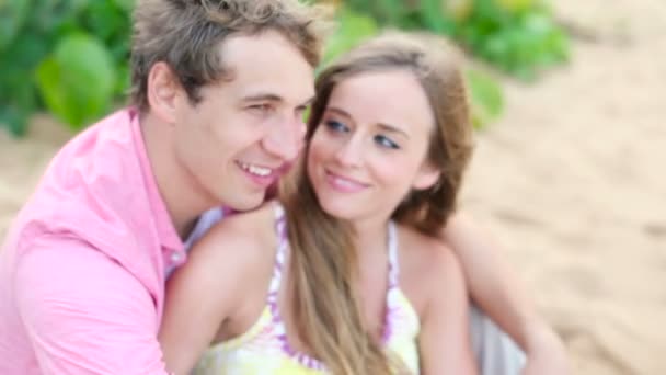 Sonriente joven pareja enamorada, sentada y abrazada en la playa — Vídeo de stock