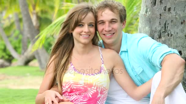 Pareja sonriente enamorada, sentada y abrazada bajo la palmera — Vídeos de Stock