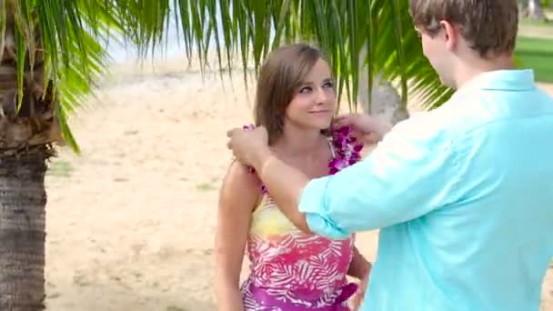 Junger Mann legt Frau am Strand Girlande aus rosa Orchideen um den Hals — Stockvideo