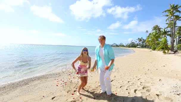 Feliz pareja joven divirtiéndose con muchos pétalos de rosa en la playa — Vídeo de stock
