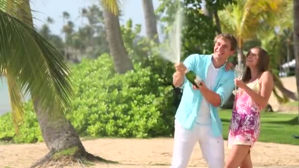 Joven pareja feliz haciendo estallar corcho de champán en la playa — Vídeo de stock