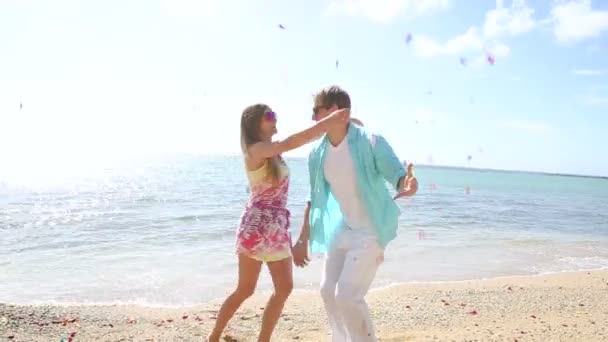 Glückliches junges Paar amüsiert sich am Strand mit vielen Rosenblättern — Stockvideo