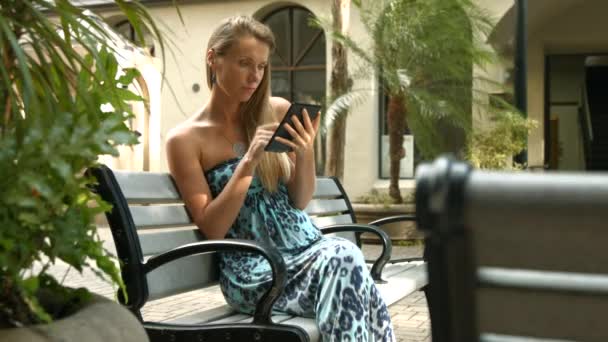 4k, Jovem, bela mulher leitura ebook sentado no banco na cidade — Vídeo de Stock