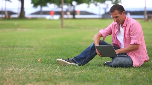 Zrelaksowany człowiek za pomocą komputera w parku — Wideo stockowe