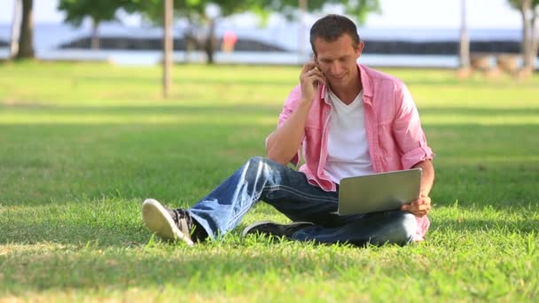 Człowiek z laptopa rozmowy na telefon komórkowy w parku — Wideo stockowe