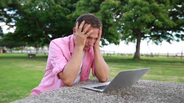 Ένας άνθρωπος κουρασμένος με υπολογιστή έχοντας πονοκέφαλος στο πάρκο — Αρχείο Βίντεο