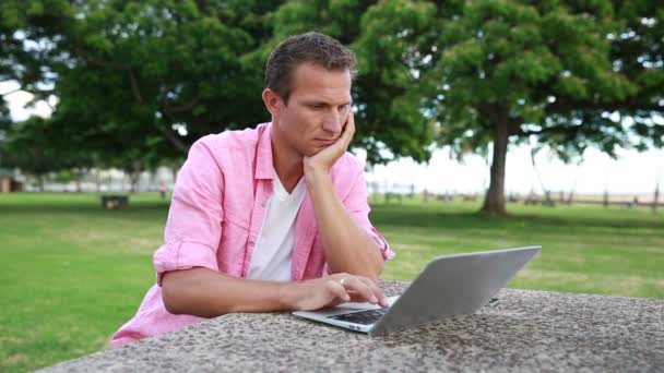 Hombre cansado con computadora teniendo dolor de cabeza en el parque — Vídeo de stock