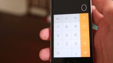 Adam akıllı telefonun hesap makinesiyle aritmetik operasyon yapıyor.