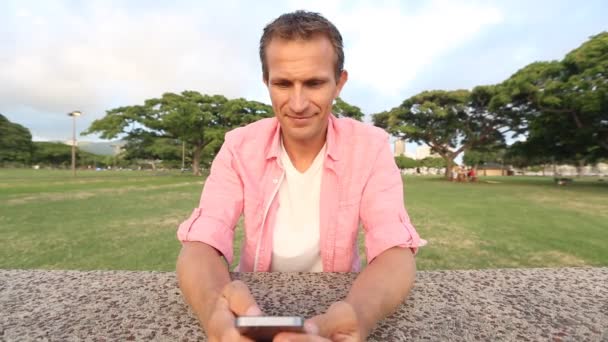 Szczęśliwy młody człowiek za pomocą smartfona w parku — Wideo stockowe