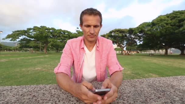 Hombre joven feliz usando Smartphone en el parque — Vídeos de Stock