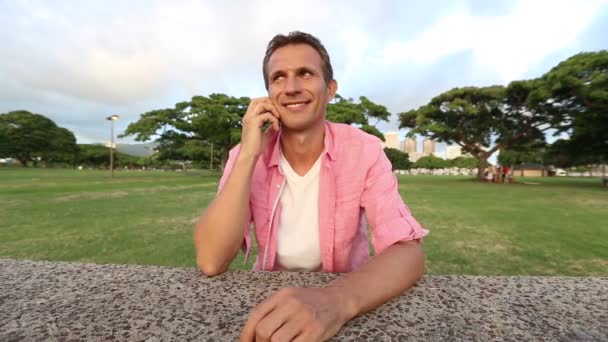 Молодий щасливий чоловік розмовляє по мобільному телефону в парку — стокове відео