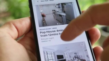 AirBnB kullanıcısı akıllı telefonundaki AirBnB uygulamasını kullanarak kalacak yer arıyor, 4K Video.
