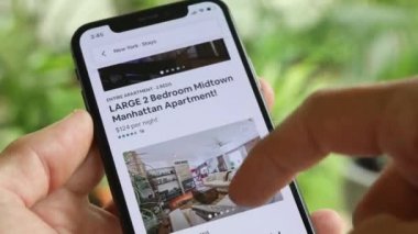 AirBnB kullanıcısı akıllı telefonundaki AirBnB uygulamasını kullanarak kalacak yer arıyor, 4K Video.