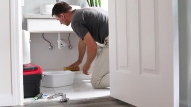 Tuvalette sızan borudan dolayı evdeki adam su temizliyor. Adam banyo zeminine su siliyor.