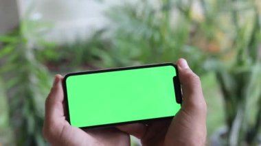 Krom tuşlu yeşil ekranlı akıllı telefonu izleyen adam. Akıllı telefon kullanan bir adam cep telefonunda yeşil ekran seyrediyor. Çevrimiçi krom tuşlara bakıyor. Sosyal medyayı okumaktan keyif alıyor.