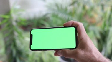 Krom tuşlu yeşil ekranlı akıllı telefonu izleyen adam. Akıllı telefon kullanan bir adam cep telefonunda yeşil ekran seyrediyor. Çevrimiçi krom tuşlara bakıyor. Sosyal medyayı okumaktan keyif alıyor.