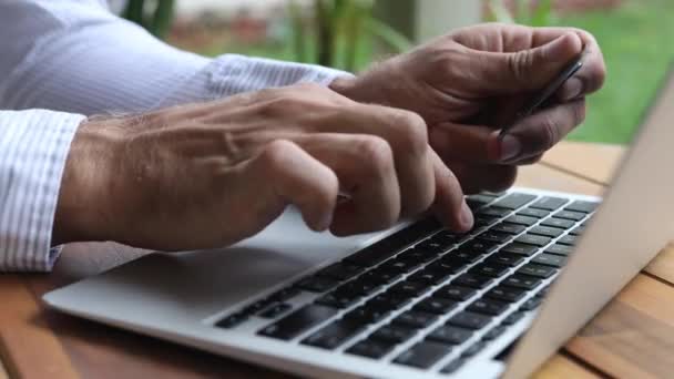 男人手握信用卡 使用智能手机 在笔记本电脑上打字 在家网上购物 网上购物付款的概念 — 图库视频影像