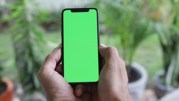 クロマキーグリーンスクリーンでスマートフォンを見ている男 携帯電話の閲覧に緑の画面を見てスマートフォンを使用して男クロマキーをオンラインで自宅でソーシャルメディアを読んで楽しんで閉じる手 — ストック動画