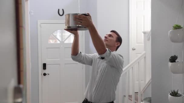 天井から水が流れる鍋を持っている男 天井から水が漏れている間に動揺した男がポットを保持し 家は改装が必要です — ストック動画
