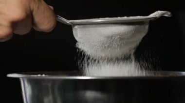 Elle yapılan bir kavgada un yakın plan. Un pişirme işi. Yavaş hareket eden erkek elleri kase içinde süzgeçten un seçiyor.