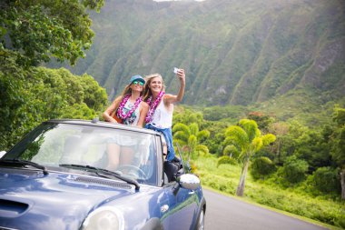 Araba yolculuğu tatilinde gençler yaz tatili sırasında telefonlarıyla selfie çekiyorlar. Turistler, Hawaii 'de üstü açık arabalarla fotoğraf çekiyorlar, akıllı telefon kameralarıyla.