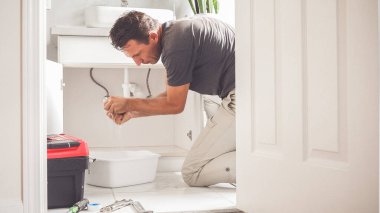 Tesisatçı banyonun zeminine su döker. Tuvalette sızıntı yapan borudan su temizleyen adam.