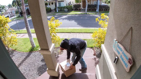 Paket hırsızı video kapı zili sisteminde bir banliyö evinin kapısından kutu teslimatı çalarken yakalandı.