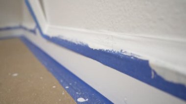 Kalıptan bant çıkarılıyor. Bir ressam, temiz kenar bir süpürgelik ortaya çıkarmak için duvardan mavi boyacının bandını çıkarır..